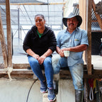 Two people sitting on a wooden platform inside a greenhouse.